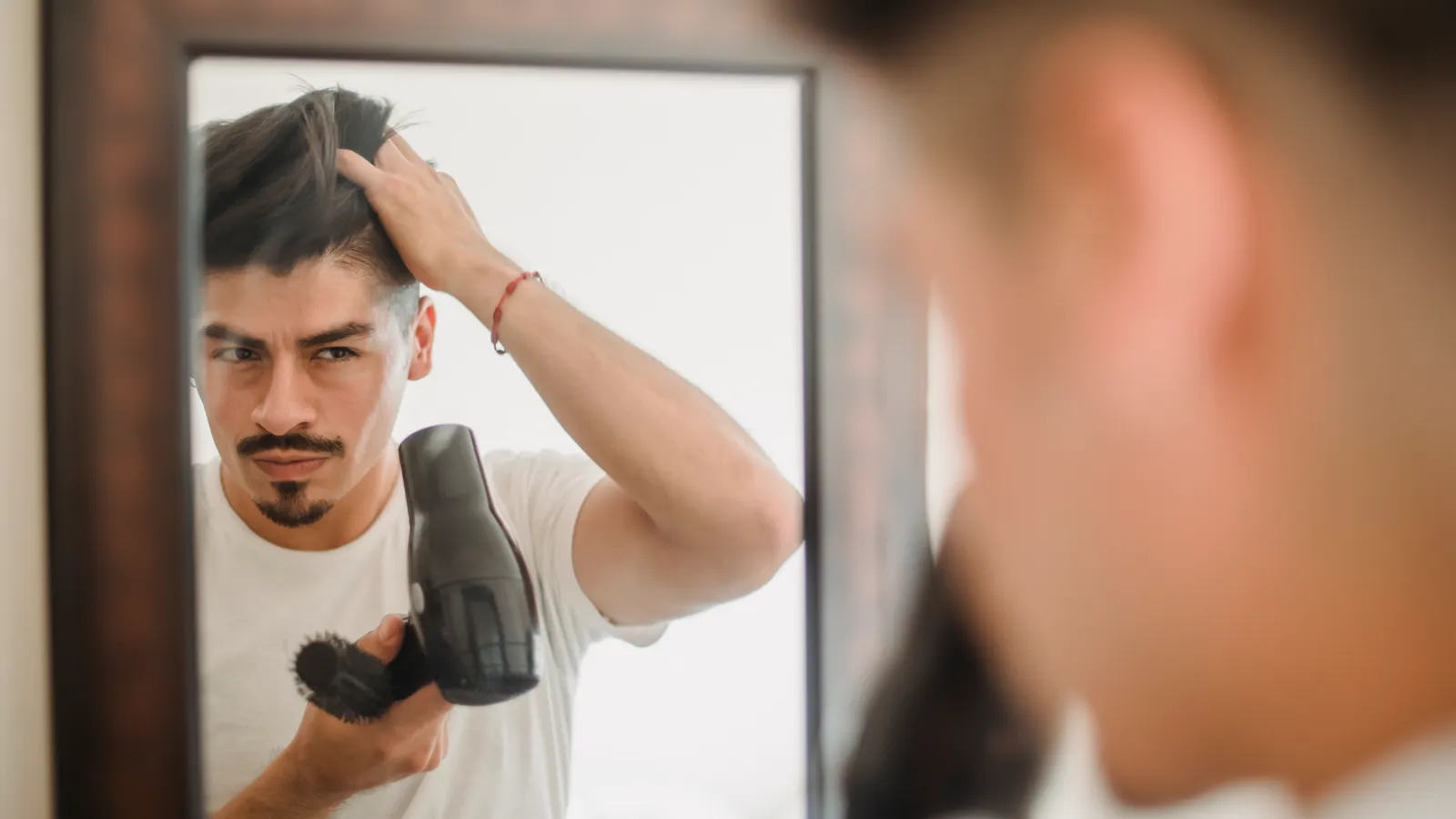 Homem secando o cabelo em frente ao espelho